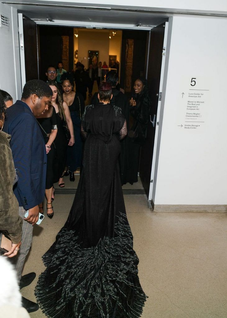 A guest walking through the Mugler exhibit, wearing a gown with a long train.