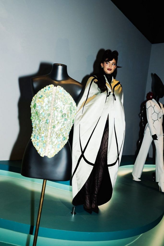 Kylie Jenner wearing an archival coat and catsuit borrowed from the exhibit, standing in place of the mannequin that wears it.