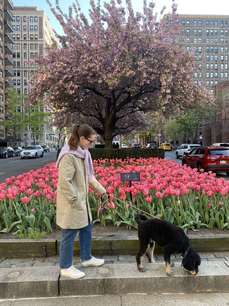 Halie walks her dog in Onitsukas, plus an Asket coat, Asket jeans, Warby Parker sunglasses, and a Mango sweater tied as a scarf.